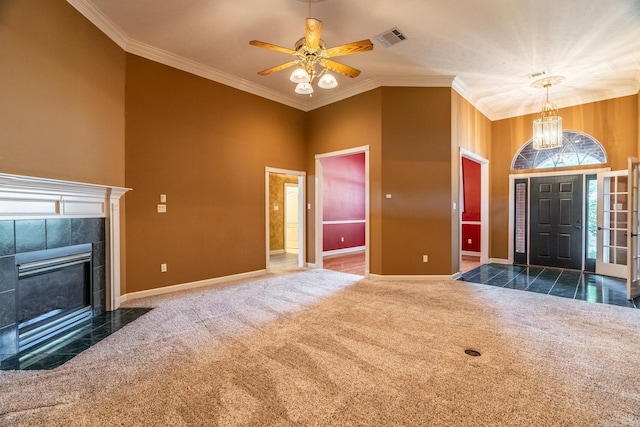 carpeted foyer entrance with a tile fireplace, a high ceiling, ceiling fan with notable chandelier, and crown molding