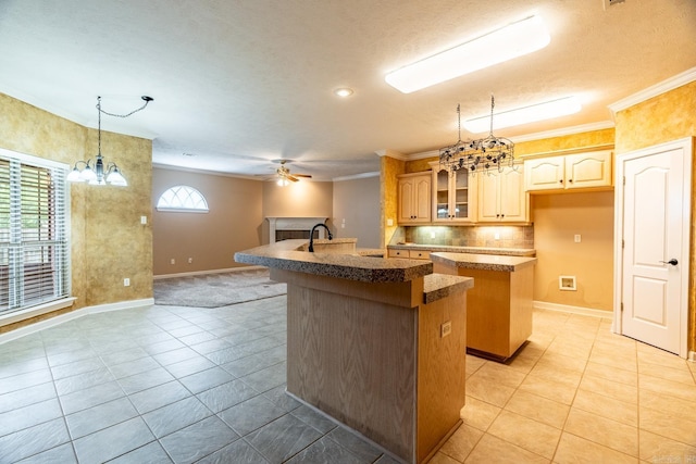 kitchen with ornamental molding, ceiling fan with notable chandelier, a kitchen island with sink, light tile patterned floors, and pendant lighting