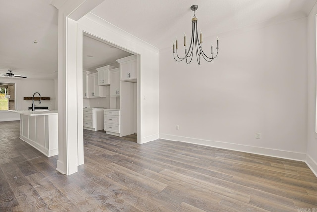 unfurnished dining area featuring dark wood-type flooring, ceiling fan with notable chandelier, and sink