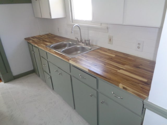 kitchen with wood counters, green cabinetry, sink, and tasteful backsplash