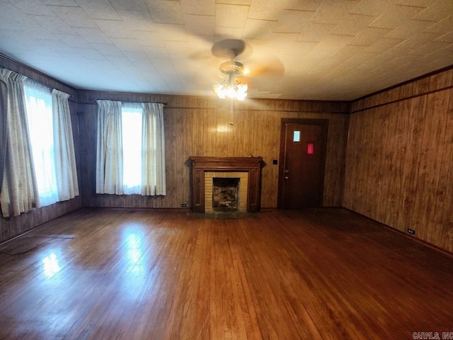 unfurnished living room featuring a brick fireplace, hardwood / wood-style floors, wood walls, and ceiling fan