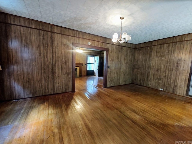 spare room with hardwood / wood-style floors, wood walls, and an inviting chandelier