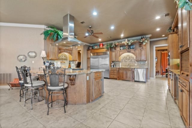 kitchen with island exhaust hood, appliances with stainless steel finishes, backsplash, and ornamental molding