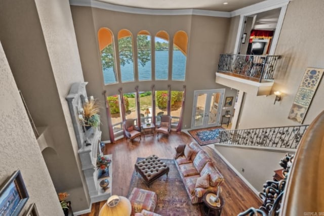 living room with french doors, ornamental molding, a water view, hardwood / wood-style flooring, and a high ceiling