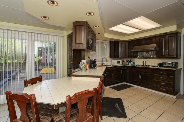 kitchen with kitchen peninsula, sink, light tile patterned floors, tile counters, and dark brown cabinets