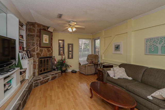 living room featuring light wood-type flooring, a textured ceiling, ceiling fan, crown molding, and a fireplace