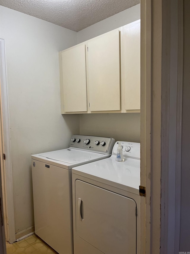 clothes washing area featuring cabinets, a textured ceiling, and washing machine and clothes dryer