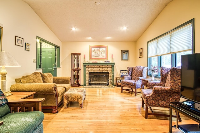 living room with a textured ceiling, light hardwood / wood-style flooring, vaulted ceiling, and a brick fireplace