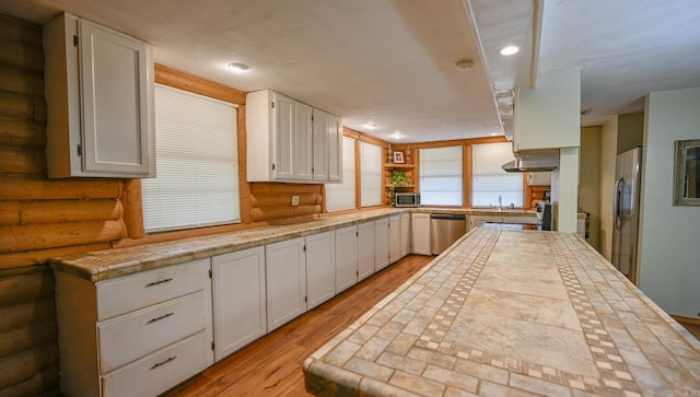 kitchen with extractor fan, white cabinets, log walls, light hardwood / wood-style floors, and stainless steel appliances