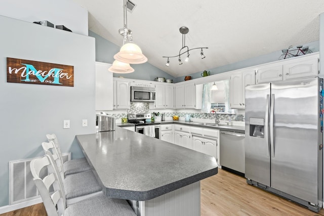 kitchen with appliances with stainless steel finishes, kitchen peninsula, white cabinets, and decorative light fixtures