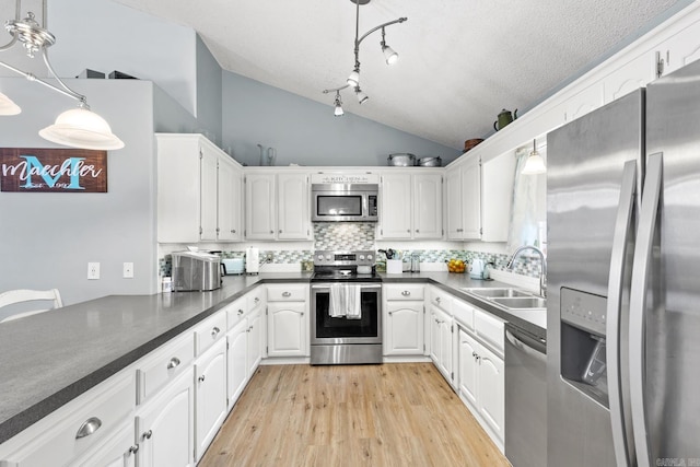 kitchen featuring lofted ceiling, sink, white cabinetry, decorative light fixtures, and appliances with stainless steel finishes