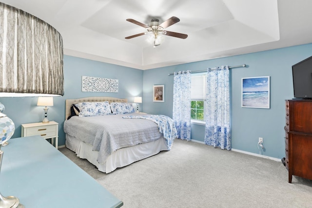 carpeted bedroom featuring ceiling fan and a raised ceiling