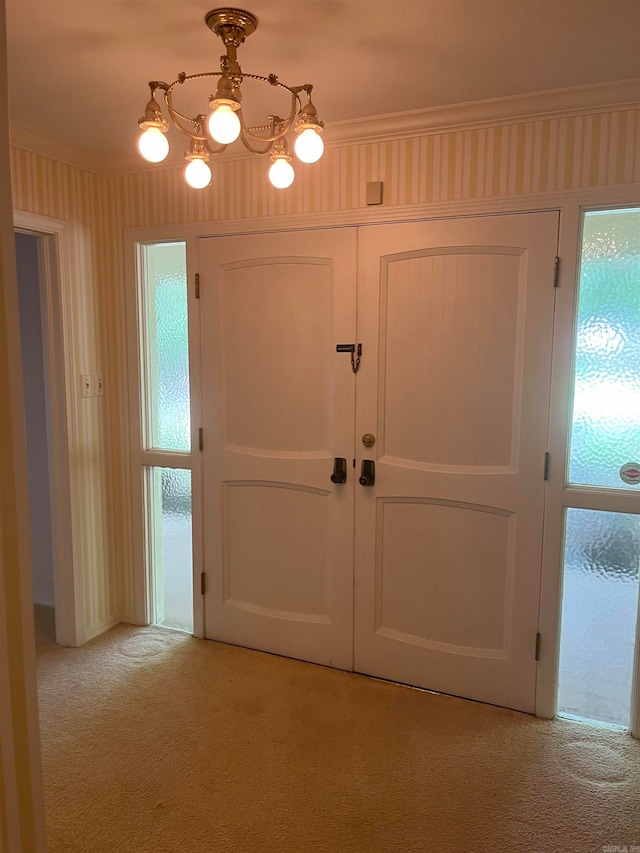 carpeted foyer with an inviting chandelier and ornamental molding