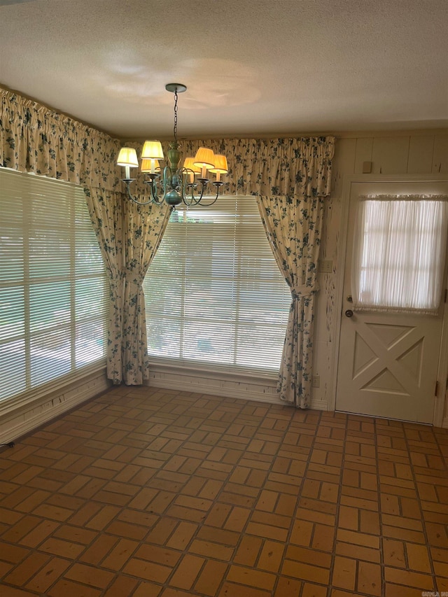 unfurnished dining area featuring a textured ceiling, a wealth of natural light, and an inviting chandelier