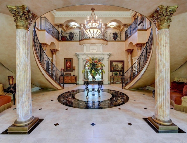 tiled foyer with a notable chandelier, ornamental molding, decorative columns, and a high ceiling