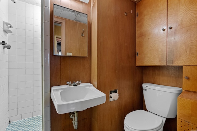 bathroom featuring tiled shower, wooden walls, toilet, and sink