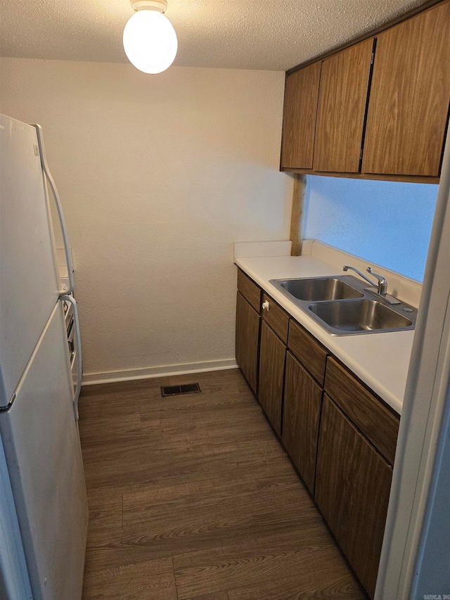 kitchen featuring sink, white fridge, a textured ceiling, and dark hardwood / wood-style floors