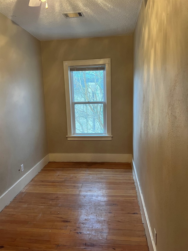 empty room with a textured ceiling and light hardwood / wood-style flooring