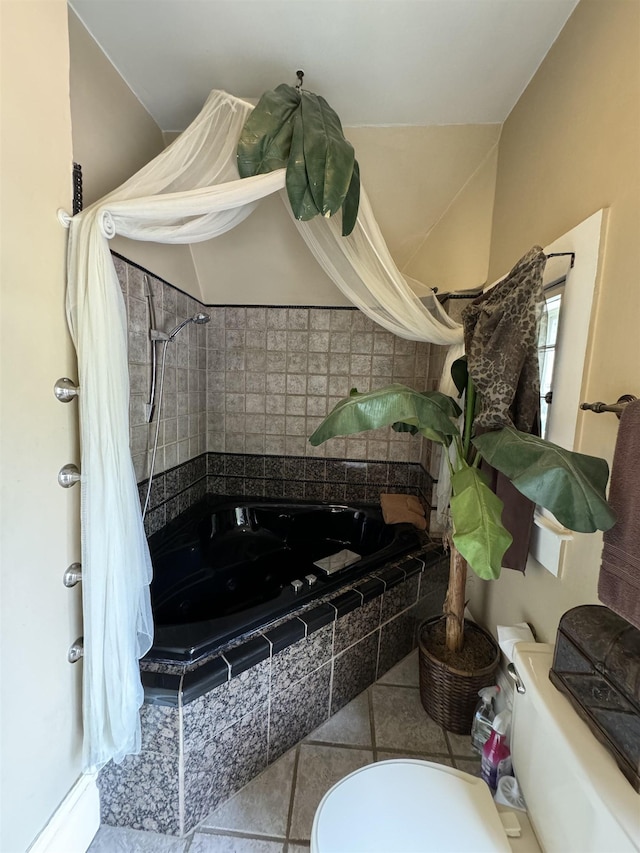 bathroom with a relaxing tiled tub, tile patterned floors, and toilet