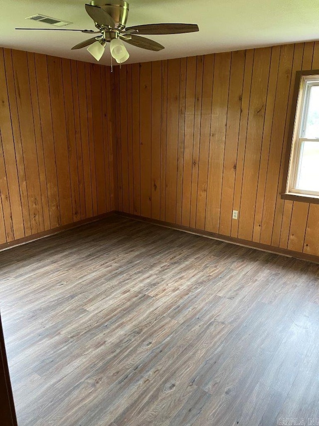 empty room with ceiling fan, wood walls, and light hardwood / wood-style flooring