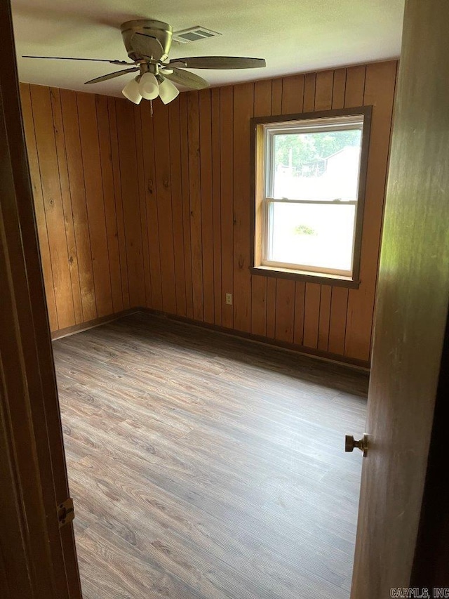 spare room with light wood-type flooring, ceiling fan, and wooden walls