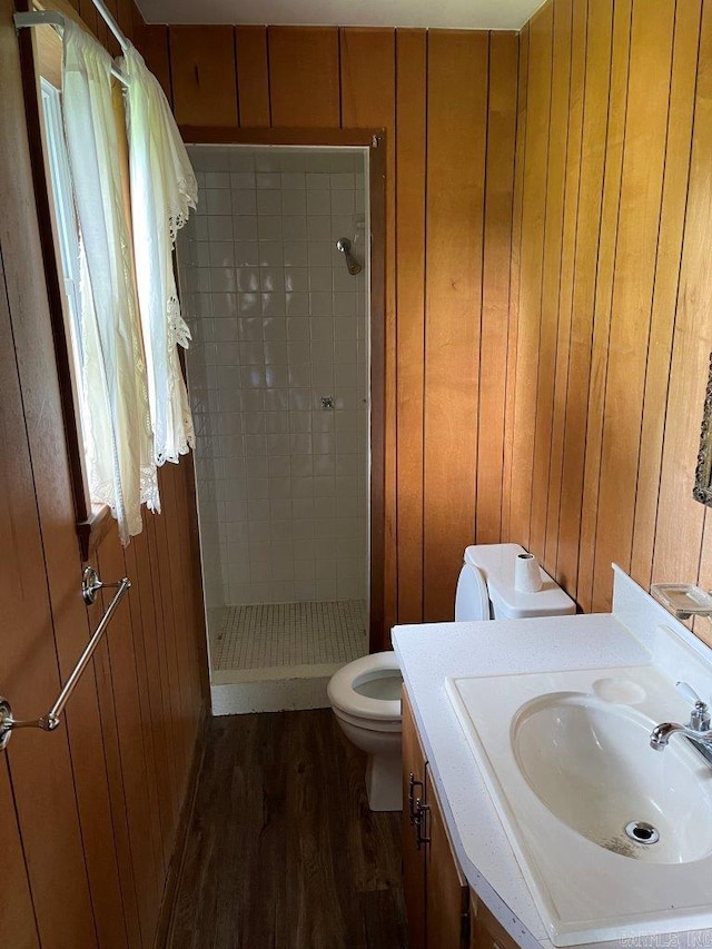 bathroom with vanity, wood walls, hardwood / wood-style flooring, toilet, and tiled shower