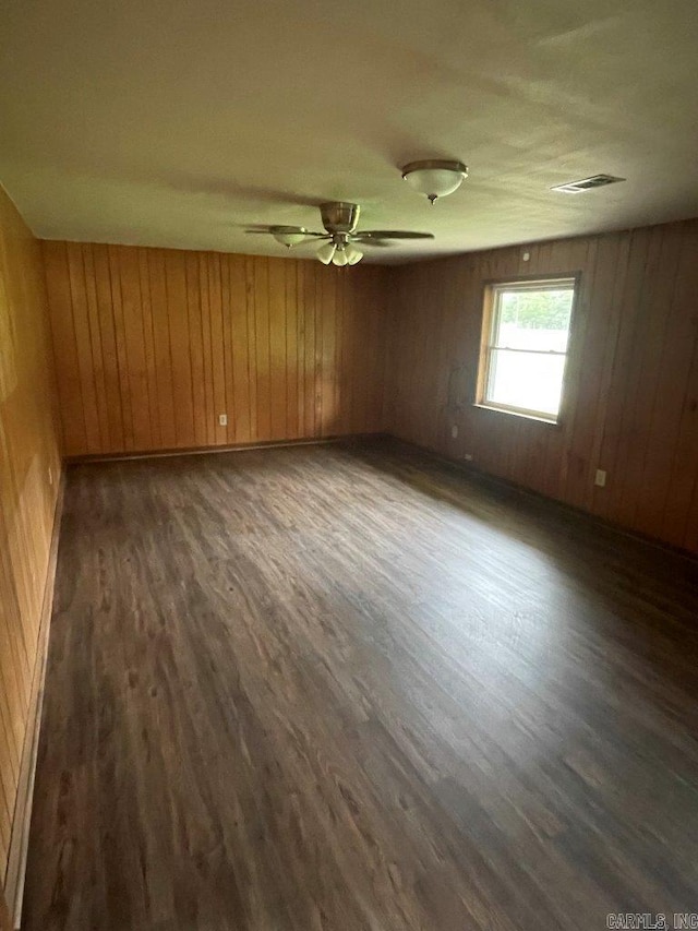 empty room featuring wooden walls, ceiling fan, and dark wood-type flooring