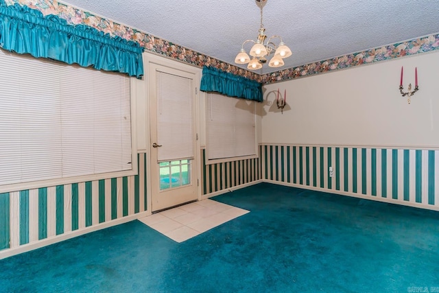 carpeted empty room featuring a textured ceiling and an inviting chandelier