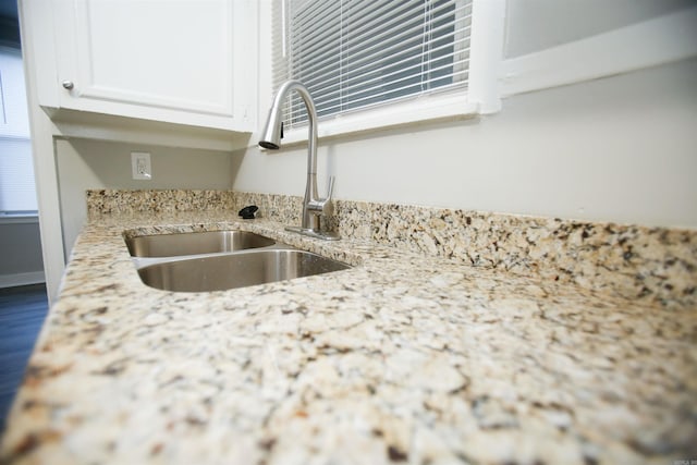 room details featuring sink, white cabinets, and light stone counters