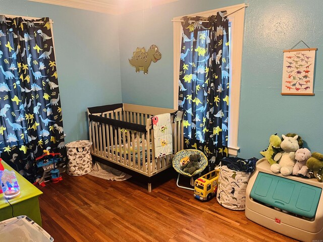 bedroom featuring ornamental molding, a nursery area, and hardwood / wood-style flooring