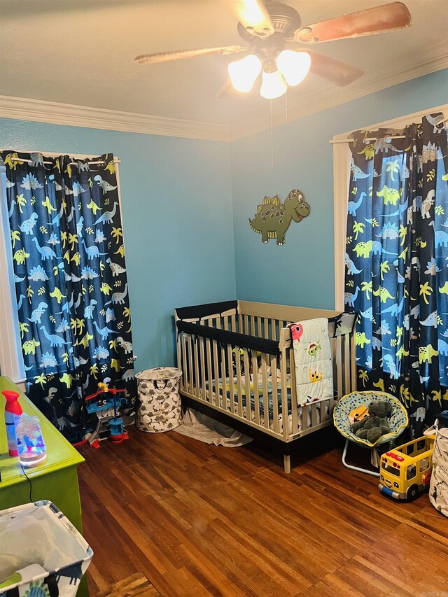 bedroom featuring a crib, ceiling fan, wood-type flooring, and ornamental molding