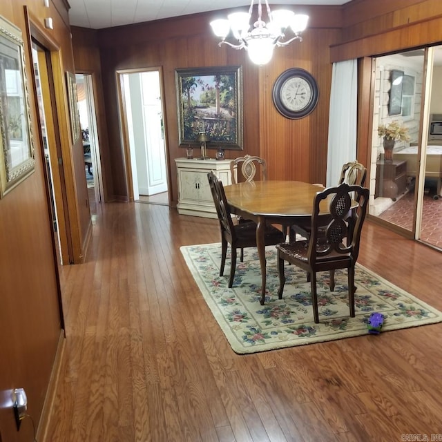 dining space featuring hardwood / wood-style flooring, wood walls, and a notable chandelier