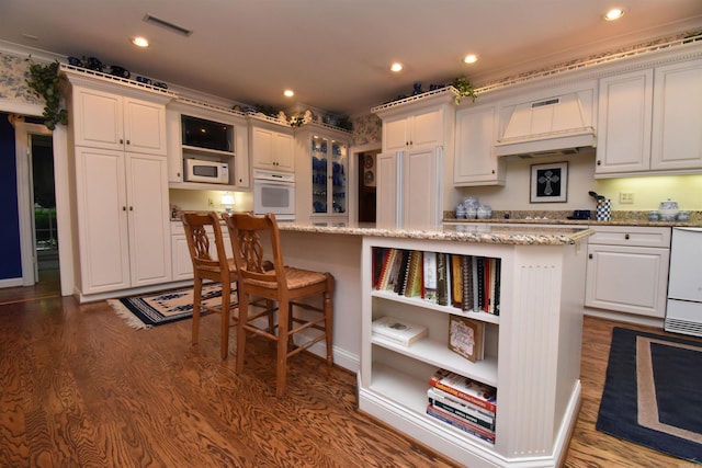 kitchen featuring white appliances, premium range hood, light stone counters, white cabinets, and a kitchen island