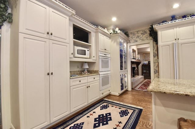 kitchen with white appliances, white cabinetry, ornamental molding, light stone countertops, and light hardwood / wood-style floors