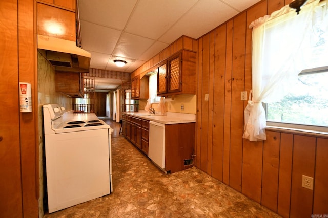 kitchen with wooden walls, dark tile patterned floors, white appliances, and a paneled ceiling