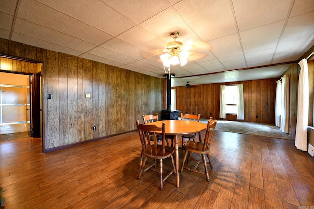 dining area with a drop ceiling, hardwood / wood-style flooring, wooden walls, and ceiling fan