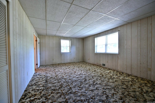 carpeted empty room featuring a paneled ceiling and wooden walls