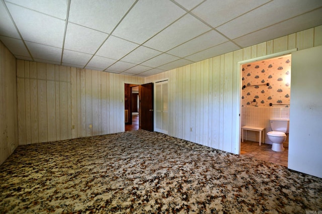 unfurnished bedroom with a closet, carpet floors, connected bathroom, and a paneled ceiling