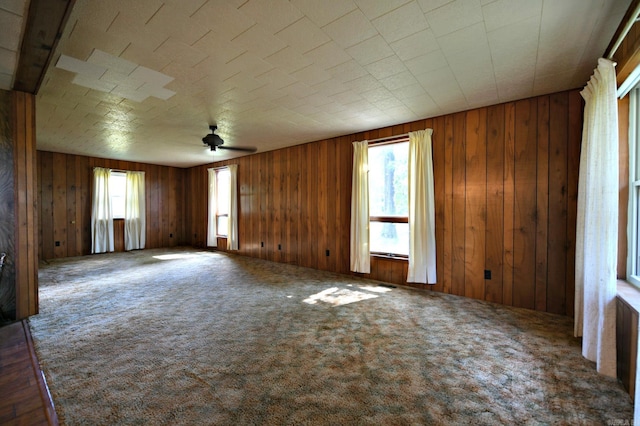 spare room with wood walls, ceiling fan, and carpet flooring