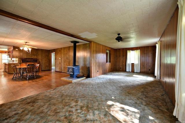 unfurnished living room featuring wood walls, carpet flooring, and a wood stove