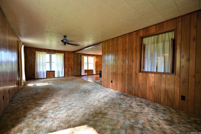 unfurnished room with carpet floors, ceiling fan, and wooden walls