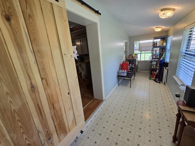 hallway featuring vaulted ceiling, a barn door, and a textured ceiling