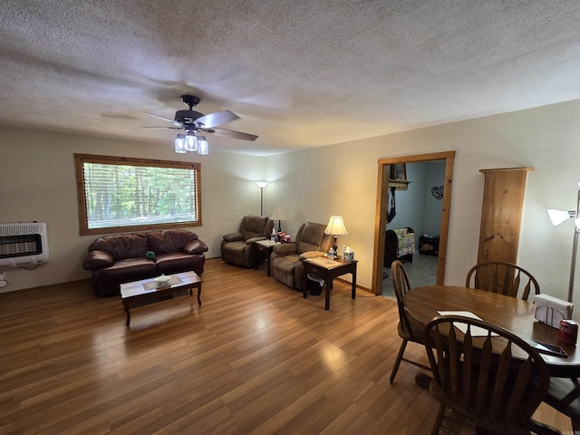 living room with heating unit, ceiling fan, wood-type flooring, and a textured ceiling