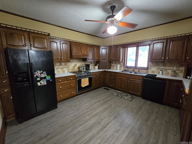 kitchen with black appliances, backsplash, sink, light hardwood / wood-style floors, and custom exhaust hood