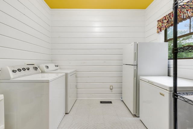 clothes washing area featuring light tile patterned floors, independent washer and dryer, and wooden walls