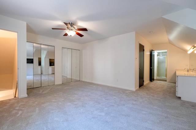 unfurnished bedroom featuring two closets, light colored carpet, and ceiling fan