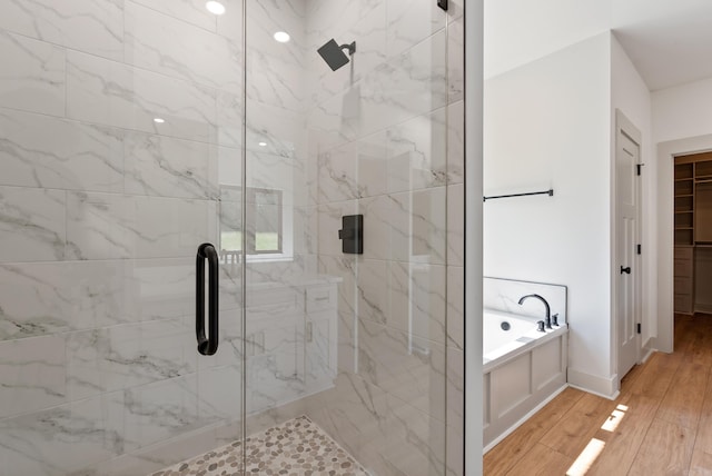 bathroom featuring baseboards, wood finished floors, a garden tub, a walk in closet, and a shower stall