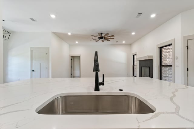 kitchen featuring recessed lighting, visible vents, open floor plan, a sink, and light stone countertops