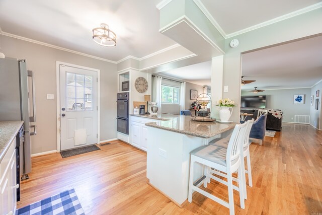 kitchen with a breakfast bar, kitchen peninsula, light wood-type flooring, light stone countertops, and ceiling fan