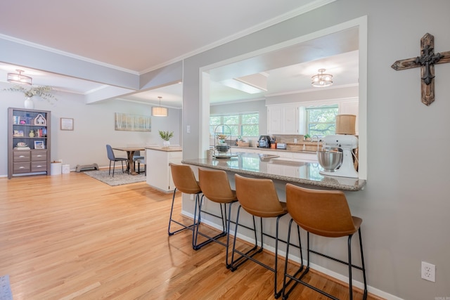 kitchen with light hardwood / wood-style floors, kitchen peninsula, a kitchen breakfast bar, and crown molding